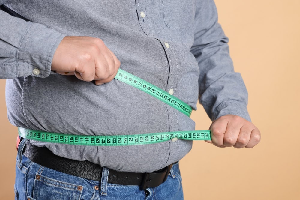A man struggling with the measuring tape for his belly fat